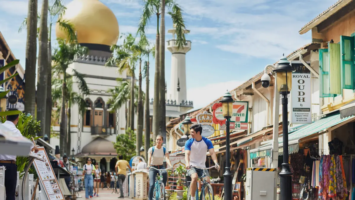 Kampong Glam — Cyclists riding past shops and restaurants on Bussorah Street below Sultan Mosque