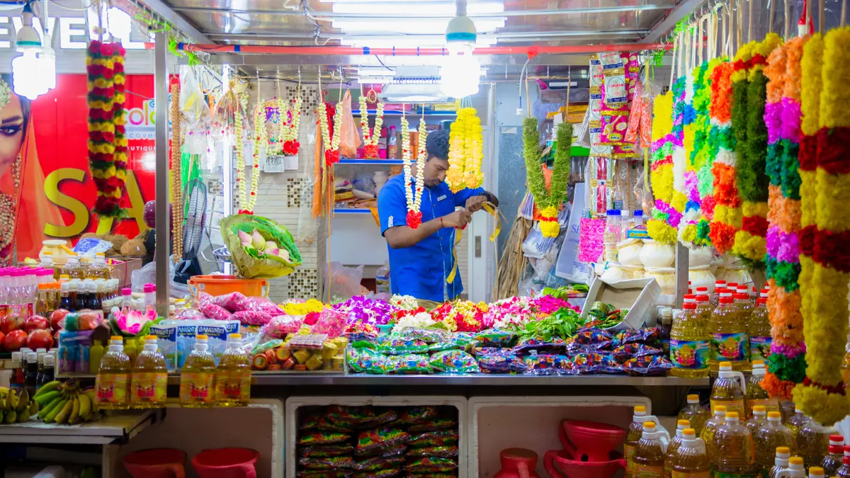 Little India — A Little India stallholder assembling flower garlands surrounded by hanging marigold and rose strings
