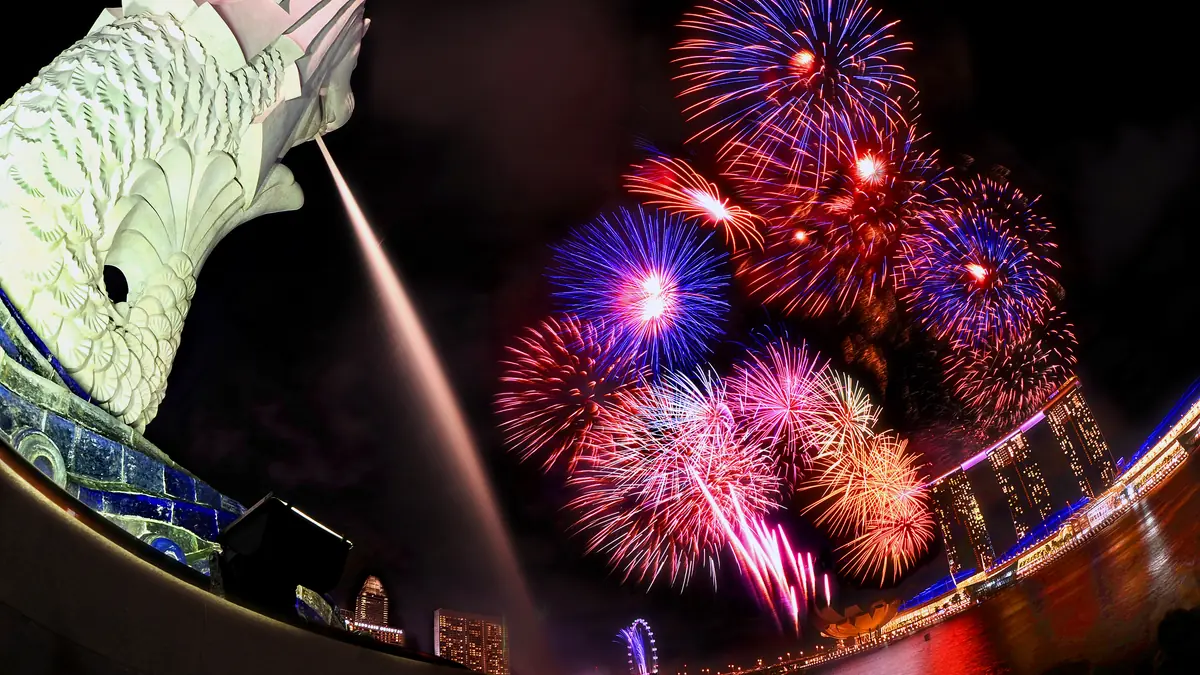 Merlion Park — Fireworks bursting over Marina Bay behind the floodlit Merlion at night