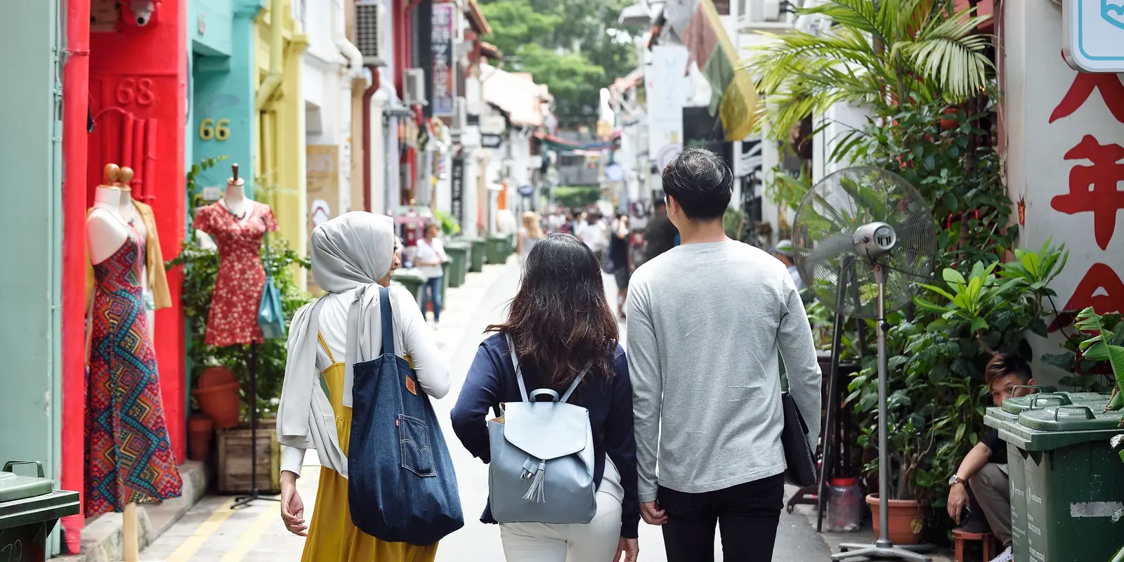 Three friends walking down Haji Lane past brightly painted shophouses and boutiques in Kampong Glam, Singapore