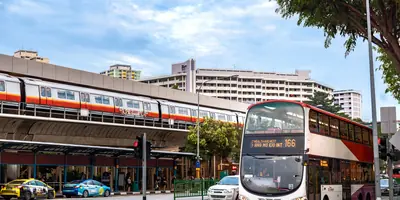 A Singapore MRT train on an elevated viaduct above a double-decker public bus and taxis on the road below